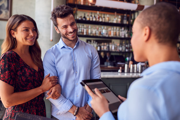 couple being greeted by maitre d using digital tab CAN8M9K